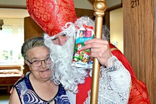 Spotkanie ze „Św. Mikołajem” 07.12.2020 Zdjęcie przedstawia Św. Mikołaja obejmującego ramieniem starszą , uśmiechnięta kobietę trzymającego pastorał i upominek – czekoladę.