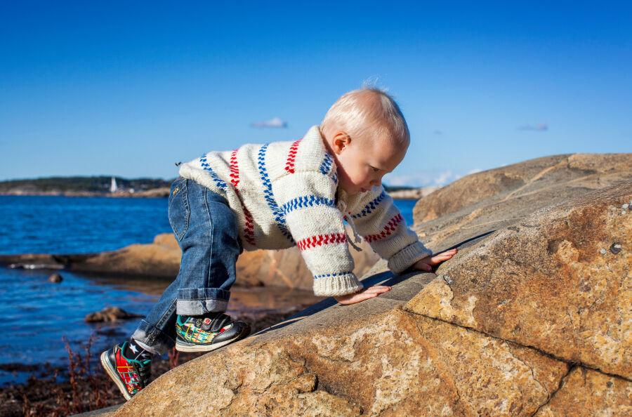 Tereny nadmorskie w pobliżu Göteborga - Kilkuletni chłopiec  wspinający się na kamień 