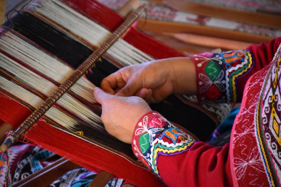 Rękodzieło Peru - zbliżenie na dłonie osoby w ludowym stroju, która tka materiał z kolorowych nici.