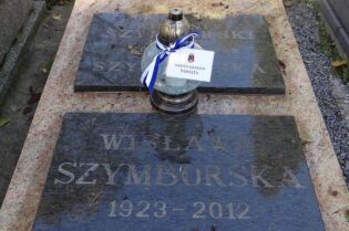 Na zdjęciu widać tablicę nagrobną Wisławy Szymborskiej (1923-2012) oraz znicz przepasany biało-niebieską wstążką z karteczką z napisem 