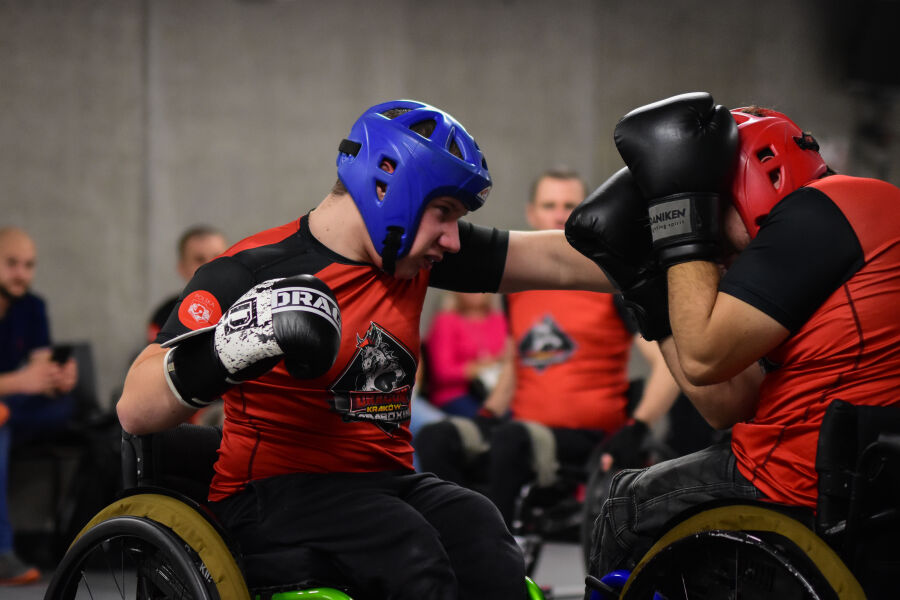 dwóch mężczyzn na wózkach walczący w sali sportowej w ochraniaczach i rękawicach bokserskich 
