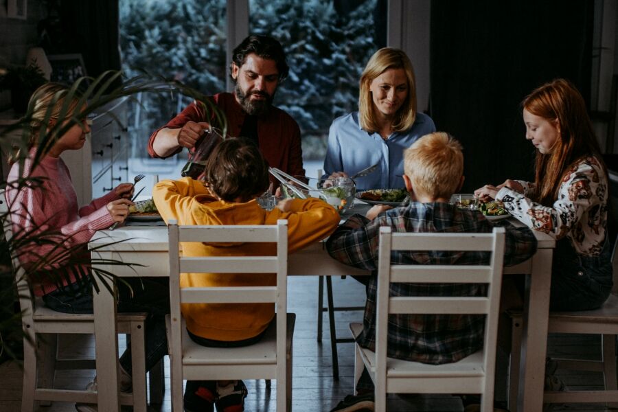 sześcioosobowa rodzina siedząca przy stole w salonie spożywa posiłek. 