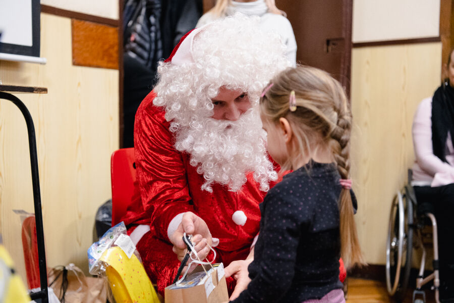 Zdjęcie przedstawia świętego Mikołaja rozdającego prezenty dzieciom z niepełnosprawnościami