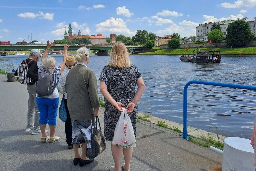 Osoby nad Wisłą i żegnają odpływający galar z widokiem na Wawel