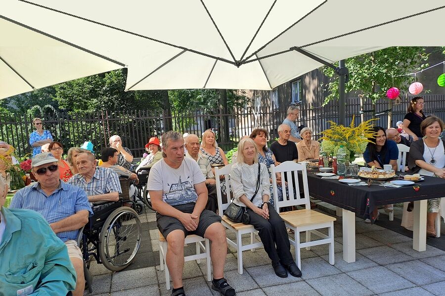 Uczestnicy siedzą pod parasolami ogrodowymi