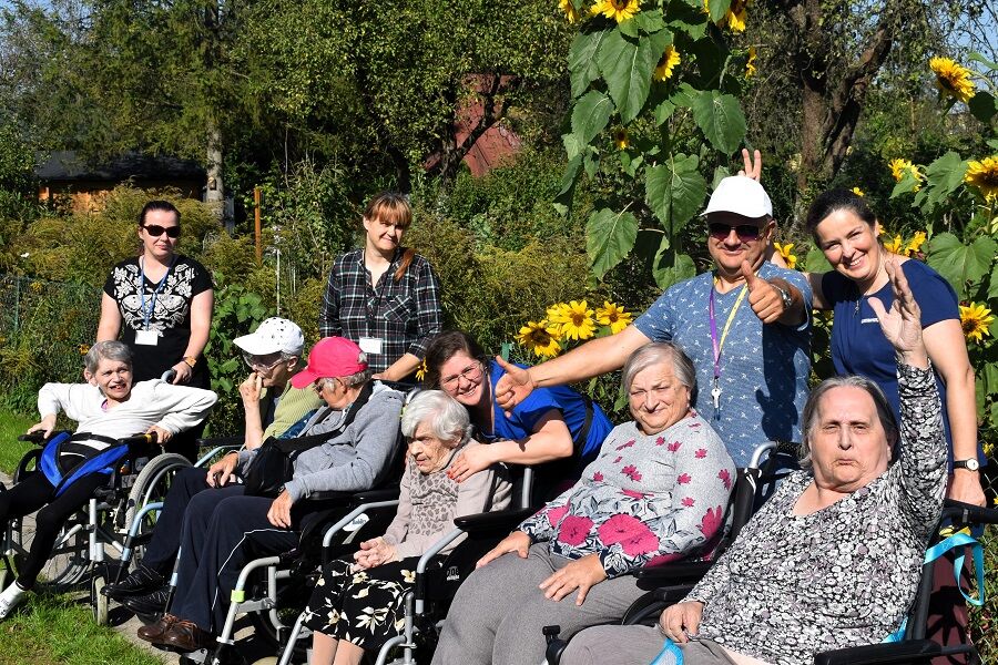 Grupa mieszkańców  opiekunami pozuje na tle pięknych słoneczników.