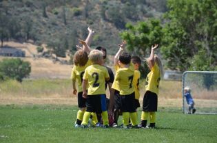 Grafika przedstawia grupkę małych dzieci, ubranych w stroje piłkarskie.