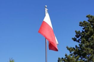 Grafika przedstawia flagę Polski powiewająca na maszcie. 