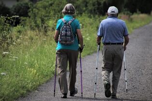 Grafika przedstawia parę seniorów uprawiających Nordic Walking.
