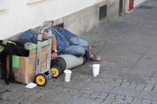 Grafika przedstawia osobę, śpiącą na chodniku na pudle kartonowym.
