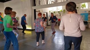 Zdjęcie przedstawia tańczących z prowadzącym seniorów podczas wydarzenia zoorganizowanego przez Fundację IB Polska