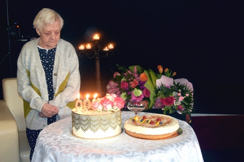 Jubilatka przy stole z urodzinowym tortem i kwiatami