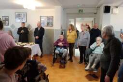 Grupa kobiet i mężczyzn w pomieszczeniu, skupionych przy odświętnie nakrytym stole.