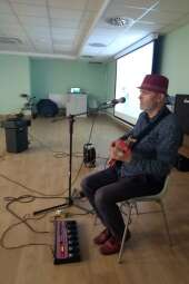 Siedzący na krześle mężczyzna z gitarą przy mikrofonie