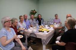 Grupa kobiet i mężczyzn w pomieszczeniu, biesiadujących przy zastawionym stole