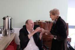 Stojąca kobieta i siedzący mężczyzna trzymający w swoich dłoniach rękę kobiety. 

