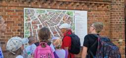 dzieci stoją z przewodnikiem przed mapą Torunia.