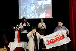 Dwójka Mieszkańców w strojach z okresu PRL trzymający flagę Solidarności