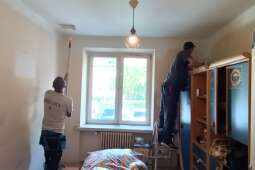 Widok dwóch pracowników wykonujących prace malarskie pokoju.