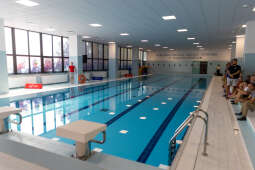 Wnętrze odnowionego basenu w Nowej Hucie podczas otwarcia. Na trybunach siedzą dzieci i dorośli, po drugiej stronie stoi ratownik. Jasna hala, niecka basenu z torami gotowa do zajęć i zawodów.