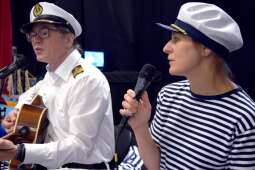 Instruktorzy w strojach żeglarskich śpiewający szanty