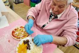 Na zdjęciu Mieszkanka układa składniki na swoją pizzę. Autor zdjęcia - pracownik DPS 