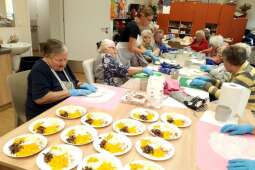 Na zdjęciu na pierwszym planie widać na talerzykach przygotowane zestawy składników do pizzy, tj.: usmażone pieczarki, ser żółty, kukurydza, cebula. 