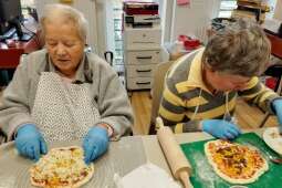 Na zdjęciu dwie Mieszkanki kończą układanie składników na swoje pizze. 