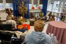 Na zdjęciu mieszkanki siedzące tyłem na tle jesiennych bukietów.