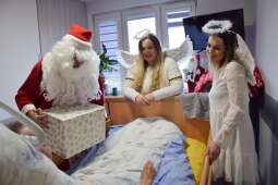 Mikołaj wraz z dwoma aniołkami przy łóżku leżącego Mieszkańca