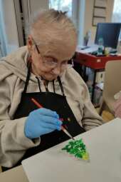 Na zdjęciu Mieszkanka maluje figurkę gipsową (choinkę). 