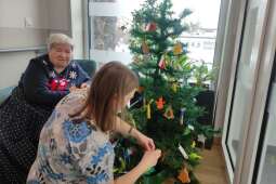 Na zdjęciu Mieszkanka wraz z terapeutką zawieszają figurki gipsowe na choinkę. 