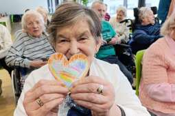 Na zdjęciu uśmiechnięta Mieszkanka wraz z serduszkiem z papieru podarowanym przez dzieci z Przedszkola Sióstr Urszulanek Unii Rzymskiej w Krakowie. 