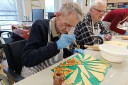 Na zdjęciu Mieszkaniec smaruje przygotowane fragmenty ciasta drożdżowego dżemem. 