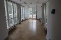 Pusty pokój z dużymi oknami i drewnianą podłogą.