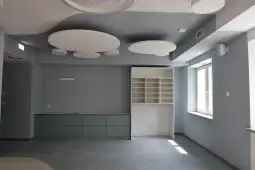 Pusty pokój z szarymi ścianami, nowoczesnym sufitem i białą zabudową meblową.