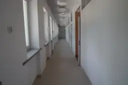 Pusty korytarz z białymi ścianami i drzwiami po obu stronach.