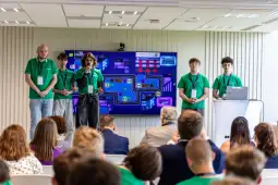 Grupa młodych ludzi prezentuje projekt przed publicznością w sali konferencyjnej.