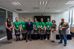 Grupa młodych ludzi w zielonych koszulkach z nagrodami i przedstawicielami instytucji.