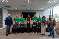 Grupa osób w zielonych koszulkach na tle sceny, z torbami w rękach, podczas wydarzenia.