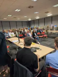 Spotkanie w sali konferencyjnej z uczestnikami i wystawionymi obrazami w tle.