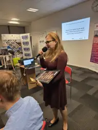 Kobieta z mikrofonem prezentuje nagrodę podczas konferencji.