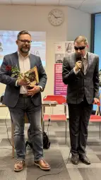 Dwaj mężczyźni na konferencji, jeden z różą, drugi z mikrofonem.