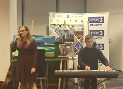 Kobieta śpiewa, mężczyzna gra na pianinie, w tle plakaty i obrazy.