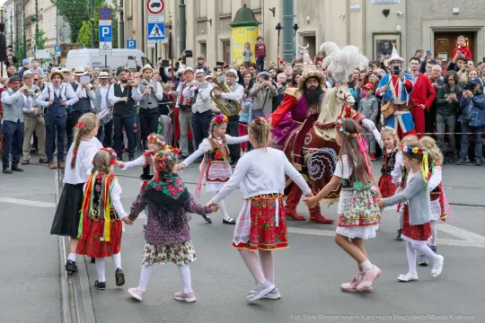 Grupa dzieci w tradycyjnych strojach tańczy w kręgu podczas festiwalu na ulicach miasta.