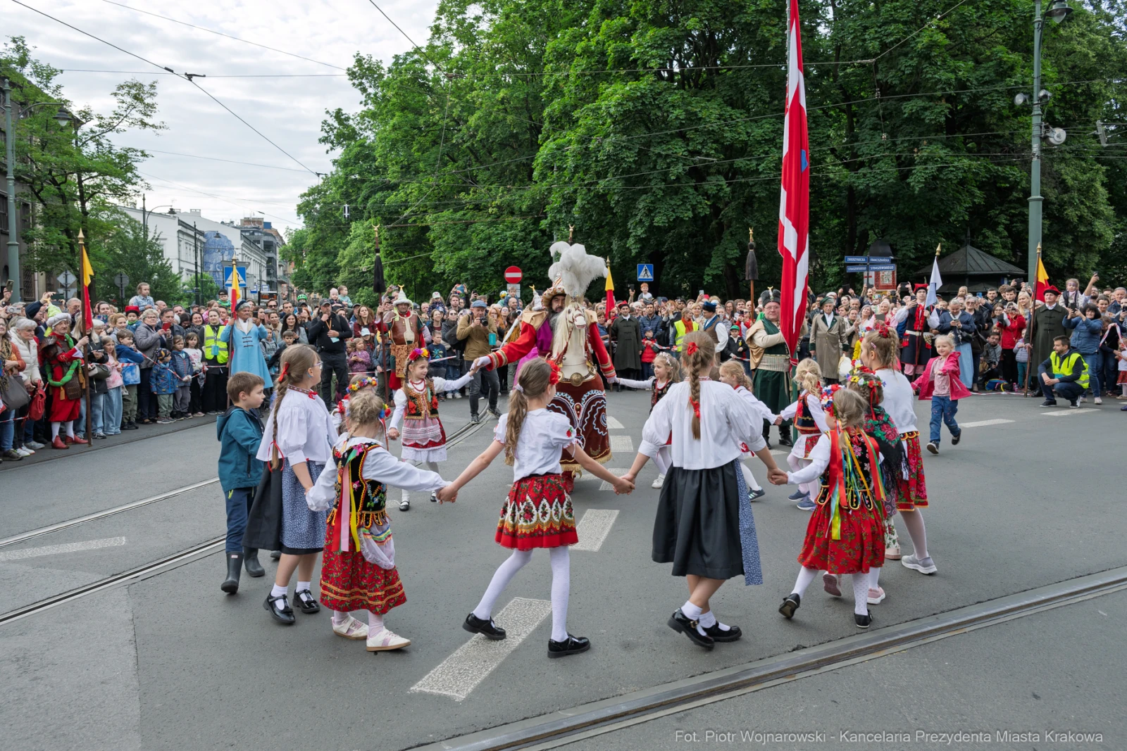 Uczestnicy parady w tradycyjnych strojach ludowych tańczą na ulicy, otoczeni tłumem widzów.  Autor: Piotr Wojnarowski