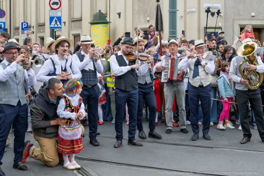 Muzycy w tradycyjnych strojach grają na instrumentach, wokół tłum ludzi i dzieci.
