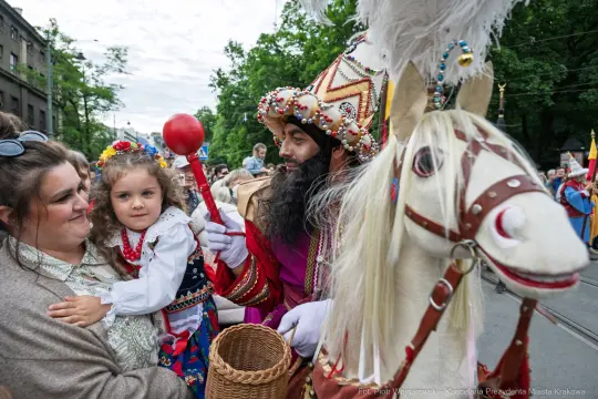 Mężczyzna w kolorowym stroju z dzieckiem w tradycyjnym ubraniu, obok konia.