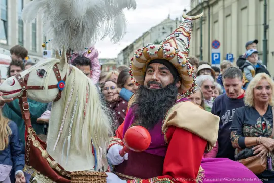 Mężczyzna w kolorowym stroju z brodą, siedzący na koniu, podczas parady w tłumie ludzi.