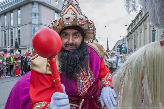 Mężczyzna w kolorowym kostiumie z koroną i berłem, uczestniczy w parady.
